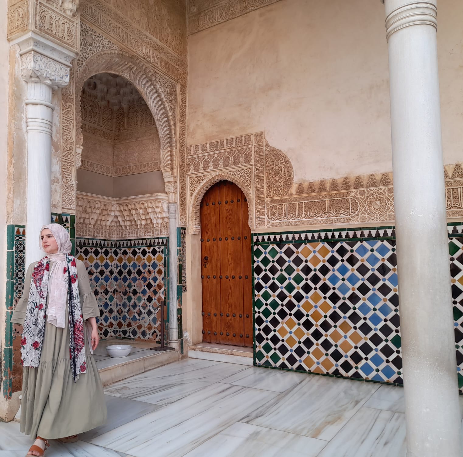 Janine Vasiliou standing in a Moorish palace courtyard of carved stone, patterned tilework and marble.